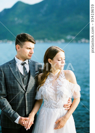 Groom hugs bride by the waist against the backdrop of mountains and the sea. Montenegro Groom hugs bride by the waist against the backdrop of mountains and the sea. Montenegro 93419659