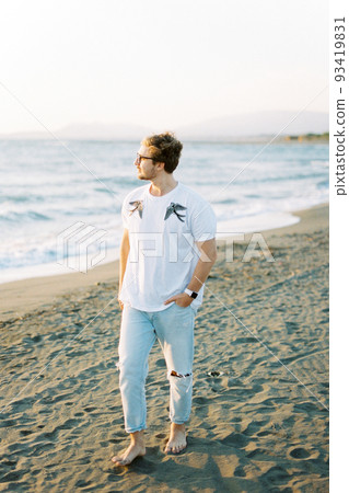 Young man walks barefoot on the beach and looks at the sea 93419831