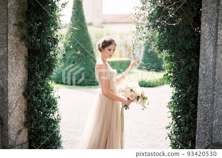 Bride with a bouquet stands against a wall covered with ivy. Lake Como, Italy 93420530