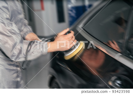 Worker polishing car with special grinder and wax from scratches at the car service station with motion blur effect 93423598