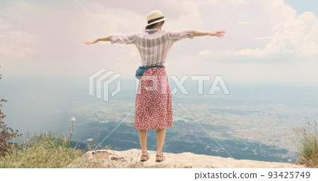 Woman traveler flaps arms like wings on mountain top. Young woman in hat opens arms wide waving like bird's wings over Tira city, Albania. Red dress happy girl blowing wind. Dream, travel concept Woman traveler flaps arms like wings on mountain top. Young woman in hat opens arms wide waving like bird's wings over Tira city, Albania. Red dress happy girl blowing wind. Dream, travel concept 93425749