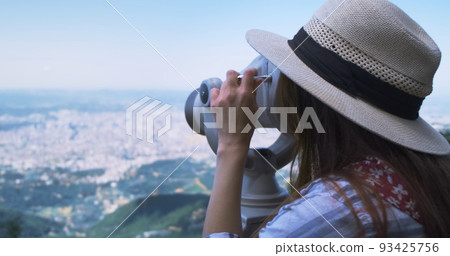 Unrecognizable woman traveler looking through viewing binoculars at summer city. Copy space. Woman observes of blur panorama, with binoculars at observation deck. Mountain Dajti Albania 93425756