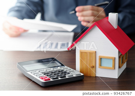 A man looking over a real estate contract. A calculator and a model house on the table. 93426767