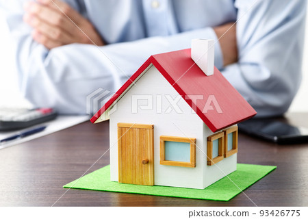 桌子上放著一個計算器和一個樣板房。一個抱著雙臂思考房地產的人。 93426775