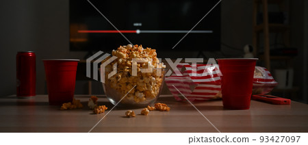Bowl of tasty popcorn and cups on wooden table in living room. Family vacation, recreation, relaxation and hobby concept 93427097