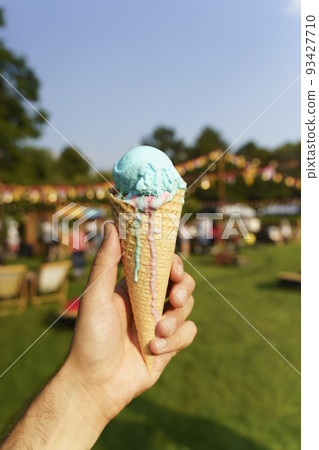 Ice cream cone in hand. Sweet dessert on summer picnic blurred background. Food, summer, ice cream concept. Selected focus Ice cream cone in hand. Sweet dessert on summer picnic blurred background. Food, summer, ice cream concept. Selected focus 93427710