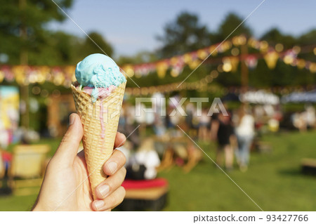 Ice cream cone in hand. Sweet dessert on summer picnic blurred background. Food, summer, ice cream concept. Selected focus 93427766