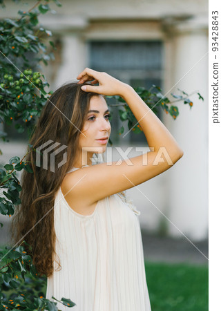portrait of a beautiful girl in a summer dress with long hair, who holds her hand in her hair, straightening it portrait of a beautiful girl in a summer dress with long hair, who holds her hand in her hair, straightening it 93428843