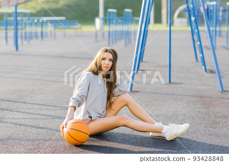 Brunette cheerful young woman dressed in casual modern clothes posing with basketball at the stadium. Brunette cheerful young woman dressed in casual modern clothes posing with basketball at the stadium. 93428848