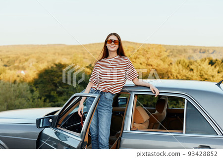 A young woman driver looks out of the car at the autumn landscape and smiles satisfactorily A young woman driver looks out of the car at the autumn landscape and smiles satisfactorily 93428852