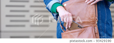 Woman putting mobile phone in brown leather handbag closeup Woman putting mobile phone in brown leather handbag closeup 93429190