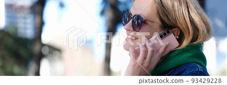 Woman in sunglasses smiling and talking on mobile phone in park Woman in sunglasses smiling and talking on mobile phone in park 93429228