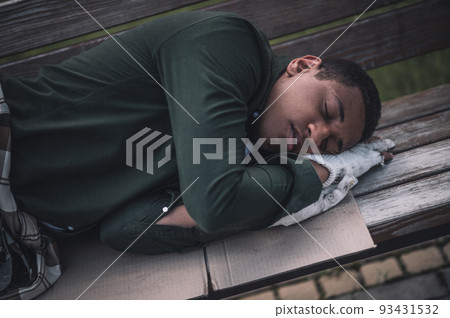 Dark-skinned man sleeping on cardboard on bench 93431532