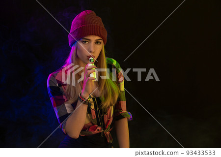 Vaping girl. Young hipster woman vape e-cig on black background. Hip-hop style. Studio shot 93433533