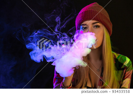 Vaping girl. Young hipster woman vape e-cig on studio on black background. Hip-hop style. Close up. 93433558