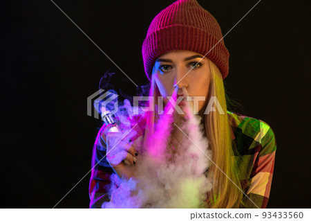 Vaping girl. Young hipster woman vape e-cig on studio on black background. Hip-hop style. Close up. 93433560