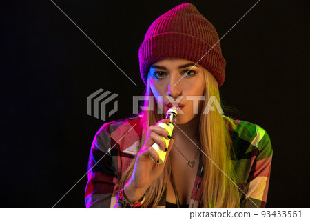 Vaping girl. Young hipster woman vape e-cig on studio on black background. Hip-hop style. Close up. 93433561