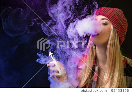Vaping girl. Young hipster woman vape e-cig on studio on black background. Hip-hop style. Close up. Vaping girl. Young hipster woman vape e-cig on studio on black background. Hip-hop style. Close up. 93433566