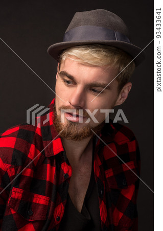 Image of attractive young bearded hipster man wearing hat dressed in shirt in a cage isolated over black background. 93433641
