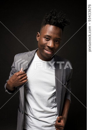 Close-up portrait of handsome black man with charming smile. Studio shot of well-dressed african guy wears white T-shirt and gray jacket. 93433676