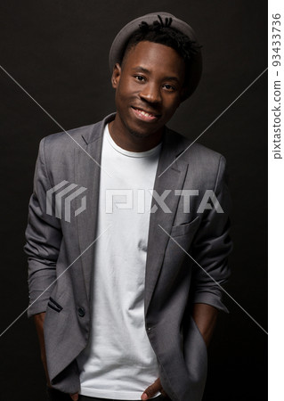 Close-up portrait of handsome black man with charming smile. Studio shot of well-dressed african guy wears hat and jacket. 93433736