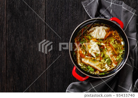 Asian Potsticker Gyoza Soup with dumpling of ground chicken, napa cabbage, green onions, ginger, celery, carrots and soy sauce in red pot on dark wooden table, flat lay, free space 93433740