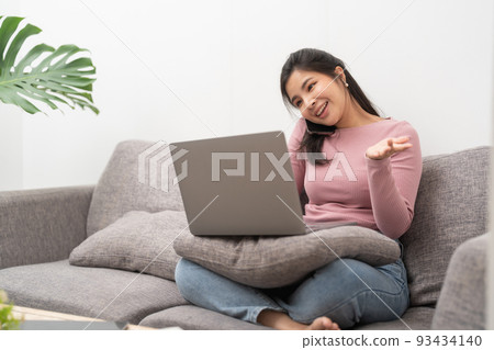 Happy young asian woman calling with mobile phone and usin laptop computer on sofa at home Happy young asian woman calling with mobile phone and usin laptop computer on sofa at home 93434140