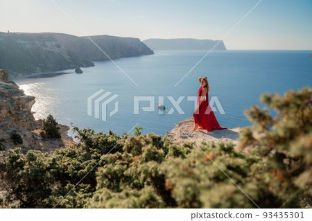 A woman in a red flying dress fluttering in the wind, against the backdrop of the sea. 93435301