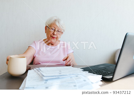 Mature editor reading printed text, making notes, using laptop, working from home, drinking coffee tea Mature editor reading printed text, making notes, using laptop, working from home, drinking coffee tea 93437212