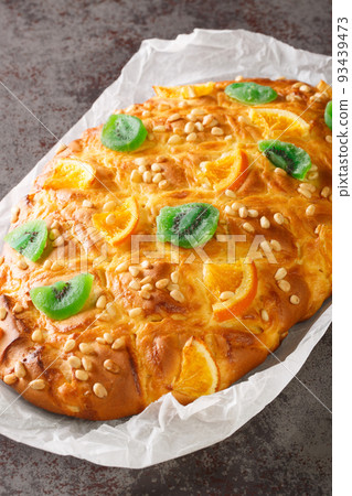 Coca de Sant Joan is one of the most popular coques, yeast breads, in Catalonia with cream and decorated with pine nuts, candied fruit closeup on the paper. Vertical Coca de Sant Joan is one of the most popular coques, yeast breads, in Catalonia with cream and decorated with pine nuts, candied fruit closeup on the paper. Vertical 93439473