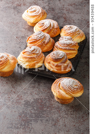Modern pastry cruffins croissants in the form of a muffin sprinkled with powdered sugar on a dark background closeup in the muffin pan. Vertical Modern pastry cruffins croissants in the form of a muffin sprinkled with powdered sugar on a dark background closeup in the muffin pan. Vertical 93439488