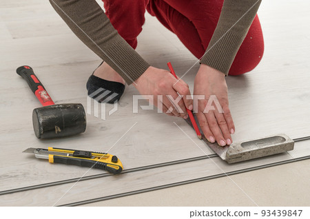 Female master draws a pencil line on a blackboard, installing quartz vinyl flooring. Female master draws a pencil line on a blackboard, installing quartz vinyl flooring. 93439847