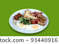 Side view of a plate with scrambled eggs, bacon, beans, sausages, tomatoes and croutons on a green background. 93440916