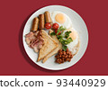 A plate with scrambled eggs, bacon, beans, sausages, tomatoes and croutons on a red background. 93440929