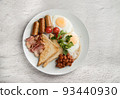 A white plate with scrambled eggs, bacon, beans, sausages, tomatoes and croutons on a light background. 93440930