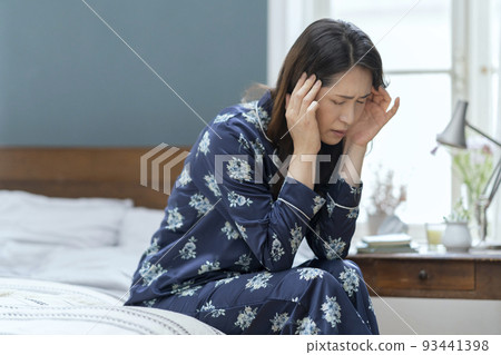Arafif woman in pajamas sitting on the bed and holding her head 93441398