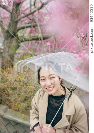 A woman looking at cherry blossoms while pointing at an umbrella on a rainy day 93443559