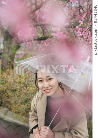 A woman looking at cherry blossoms while pointing at an umbrella on a rainy day 93443846