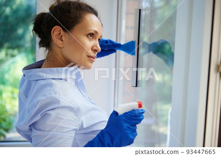Headshot beautiful housewife with gloved hands, spraying glass cleaning household chemicals and using scraper removes stains and streaks from the windows in the veranda. Cleaning. Housekeeping. Chores Headshot beautiful housewife with gloved hands, spraying glass cleaning household chemicals and using scraper removes stains and streaks from the windows in the veranda. Cleaning. Housekeeping. Chores 93447665