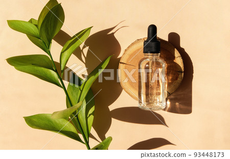Transparent glass dropper bottle with serum, oil, hyaluron on a woodcut in the sunlight with ruscus flower in soft focus. Flat lay. Natural cosmetics presentation. Testers, beauty samples perfumery. Transparent glass dropper bottle with serum, oil, hyaluron on a woodcut in the sunlight with ruscus flower in soft focus. Flat lay. Natural cosmetics presentation. Testers, beauty samples perfumery. 93448173