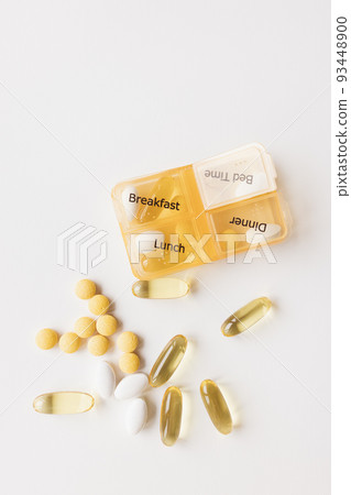 Medicine dispenser. Plastic daily box part of seven day weekly container with different white and yellow pills on white background. Top view, copy space Medicine dispenser. Plastic daily box part of seven day weekly container with different white and yellow pills on white background. Top view, copy space 93448900