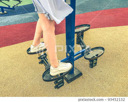 doing sports on the simulator in the park in the fresh air. a girl in a blue dress trains her legs on the platform. athlete in training doing sports on the simulator in the park in the fresh air. a girl in a blue dress trains her legs on the platform. athlete in training 93452132