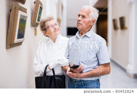 mature European couple examines paintings in an exhibition in hall of art museum 93452824