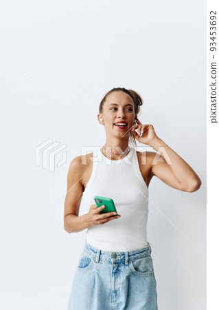 Young woman listening to music on wireless headphones through her phone and smiling at home on a white background 93453692
