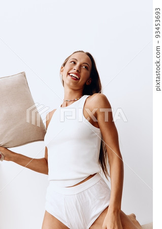 Beautiful woman in homemade white lingerie plays with couch cushions throws up with a smile and has fun. Lifestyle in a happy home and fun time Beautiful woman in homemade white lingerie plays with couch cushions throws up with a smile and has fun. Lifestyle in a happy home and fun time 93453693