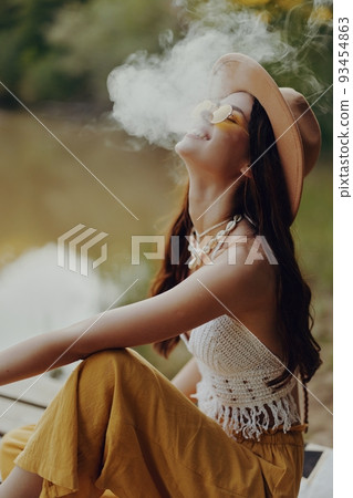 Young woman smokes wei in nature in a hippie way taking a break from the city Young woman smokes wei in nature in a hippie way taking a break from the city 93454863