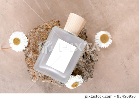 Transparent bottle of perfume with white labels on stone podium on beige terracotta background with dry flower. Top view Transparent bottle of perfume with white labels on stone podium on beige terracotta background with dry flower. Top view 93456956