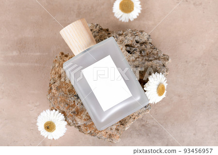 Transparent bottle of perfume with white labels on stone podium on beige terracotta background with dry flower. Top view 93456957