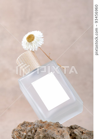 Transparent bottle of perfume with white labels on stone podium on beige terracotta background with dry flower. Transparent bottle of perfume with white labels on stone podium on beige terracotta background with dry flower. 93456960