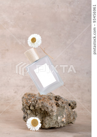 Balanced bottle of perfume with white labels on stone podium on beige terracotta background with dry flower. Balanced bottle of perfume with white labels on stone podium on beige terracotta background with dry flower. 93456961
